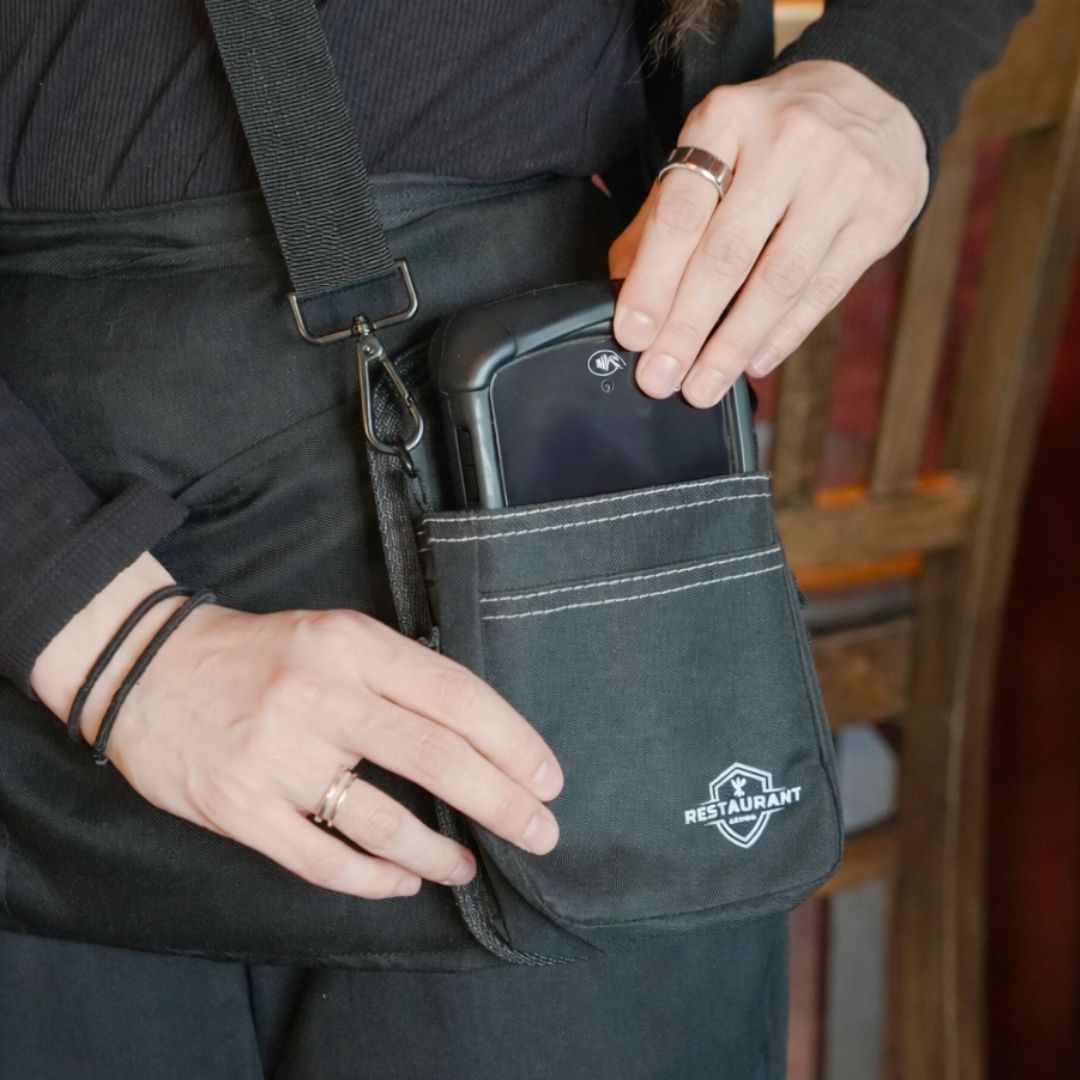 Server wearing a black Restaurant Armor POS holster while inserting a handheld POS device during service.